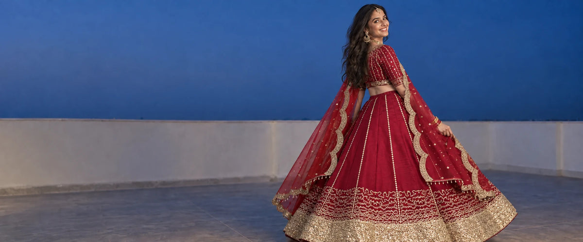Woman in a red embroidered lehenga with a net dupatta twirling on a rooftop at twilight